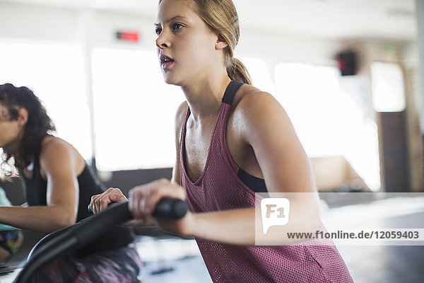 Determined young woman using elliptical bike in gym