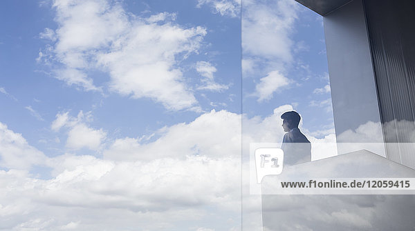 Nachdenklicher Geschäftsmann auf dem modernen Balkon mit Blick auf den blauen Himmel und die Wolken.