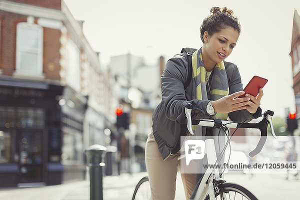 Junge Frau SMS mit Handy  Pendeln mit dem Fahrrad auf der Stadtstraße