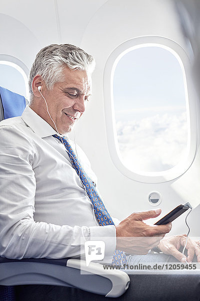 Geschäftsmann beim Musikhören mit Kopfhörer und MP3-Player im Flugzeug