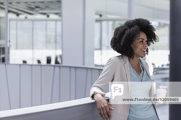 Smiling businesswoman drinking coffee at office railing