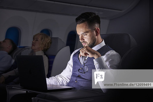 Seriöser Geschäftsmann bei der Arbeit am Laptop im Übernacht-Flugzeug