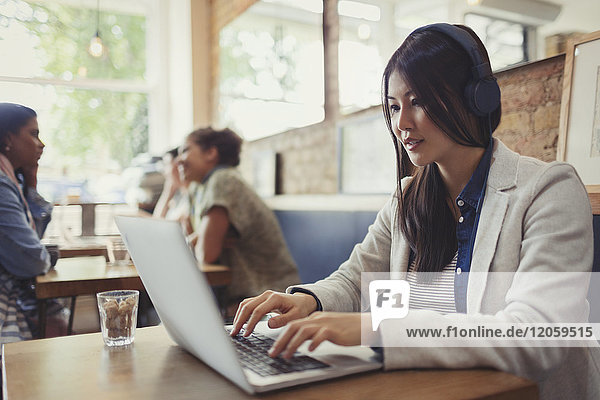 Young woman with headphones using laptop at cafe table