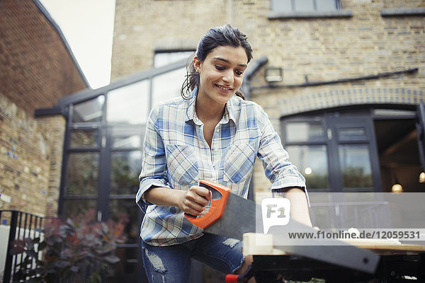 Young woman with saw cutting wood on patio