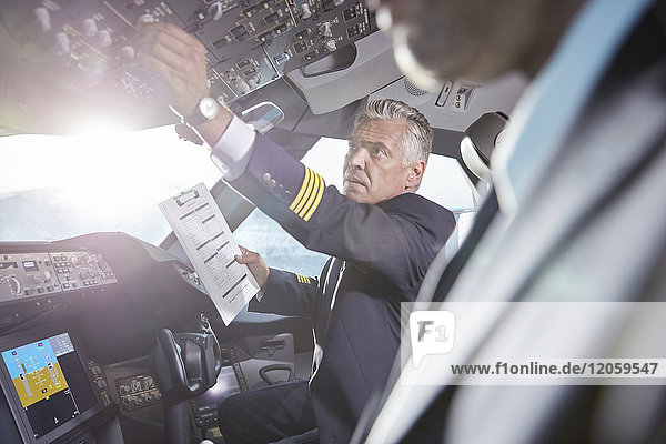 Männlicher Pilot mit Zwischenablage zur Vorbereitung und Einstellung der Instrumente im Flugzeugcockpit