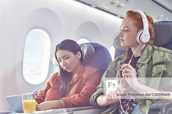 Junge Frauenfreunde mit Kopfhörer und digitalem Tablett im Flugzeug