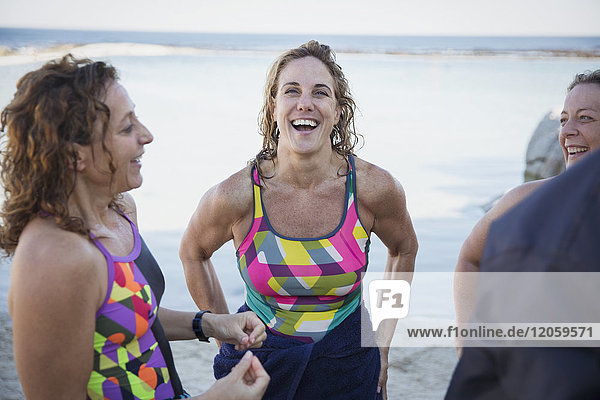 Laughing female open water swimmers talking on ocean beach