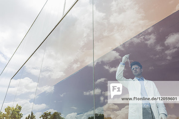 Wissenschaftler untersucht Flüssigkeit im Becherglas am modernen Fenster mit Wolkenreflexionen