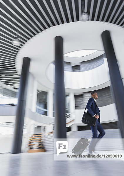 Businessman rushing  pulling suitcase in architectural  modern office lobby