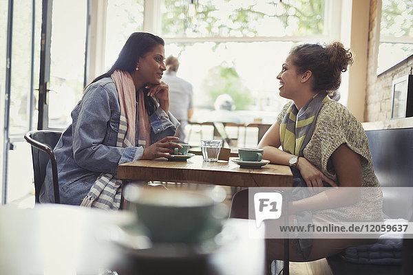 Women friends drinking coffee and talking at cafe table