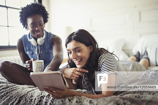 Smiling women drinking coffee and using digital tablet on bed