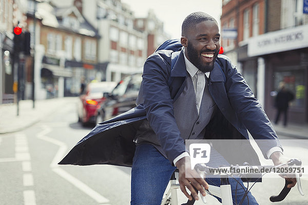 Lächelnder junger Geschäftsmann beim Pendeln  Fahrradfahren auf sonniger Stadtstraße