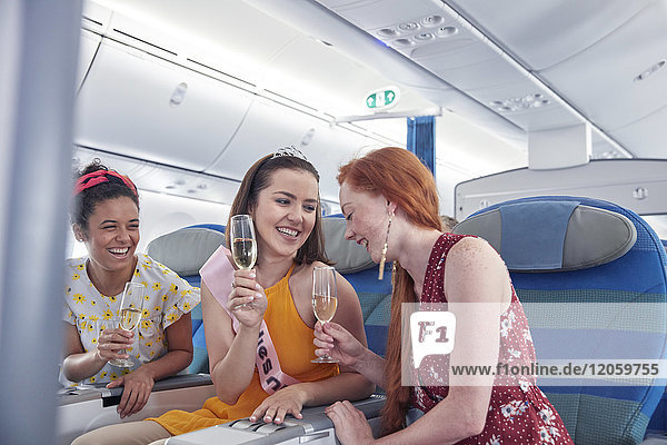 Junge Freundinnen lachend  trinken Champagner in der ersten Klasse im Flugzeug