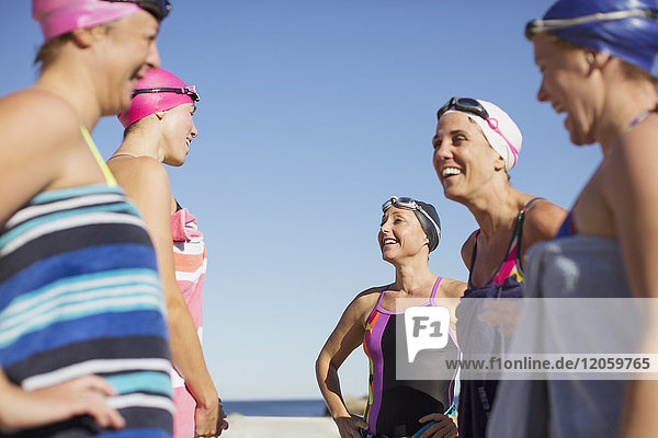 Lächelnde Schwimmerinnen sprechen am sonnigen Strand