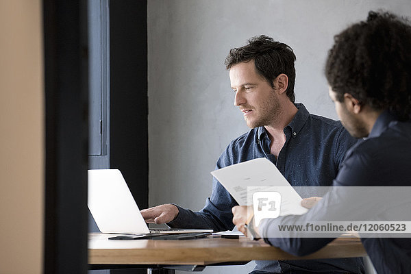 Man using laptop while other man reads document