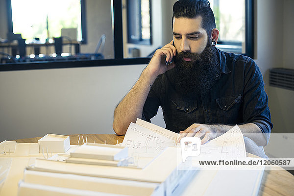 Architekt beim Betrachten von Bauplänen und beim Telefonieren im Büro