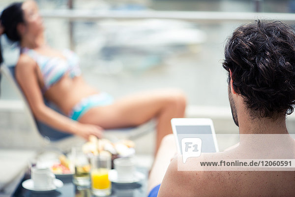 Der Mann entspannt sich am Pool mit einem digitalen Tablett