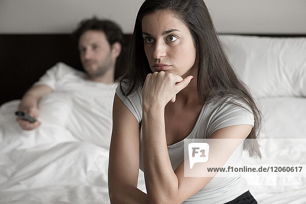 Frau sitzt im Bett  während ihr Mann fernsieht.