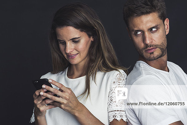 Mann  der über die Schulter blickt  wenn seine Freundin ein Smartphone benutzt.