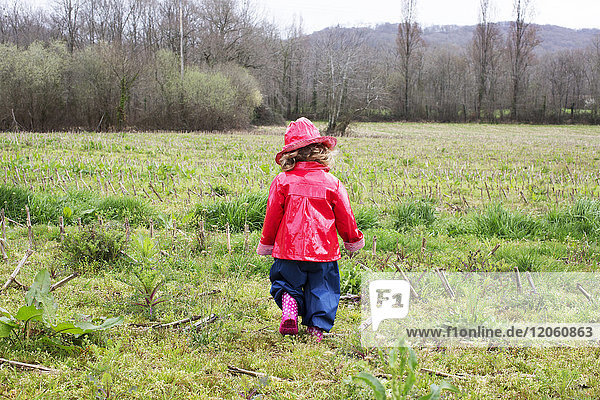 Little girl wearing rain gear playing in field