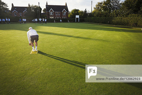 A lawn bowls player standing on a small yellow mat preparing to deliver a bowl down the green  the smooth grass playing surface.