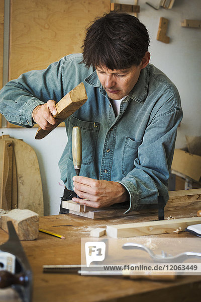 Ein Handwerker  der ein Stück Holz am Ende eines Stemmeisens benutzt  um ein Stück Holz zu markieren.