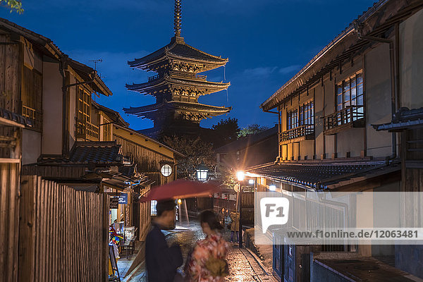 Japanisches Paar in traditioneller Kleidung  das nachts auf einer Straße steht  im Hintergrund eine Pagode.