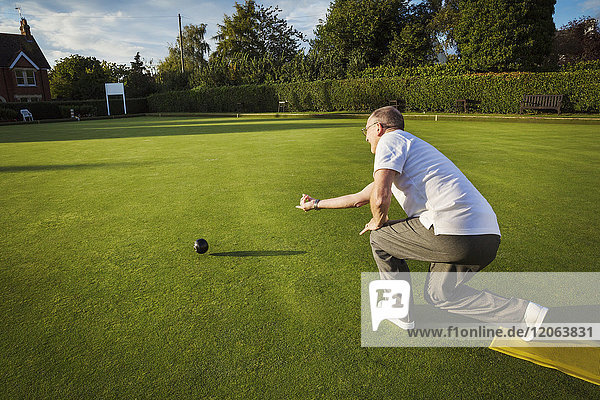 A lawn bowls player standing on a small yellow mat preparing to deliver a bowl down the green  the smooth grass playing surface.