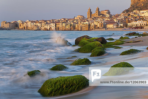 Blick entlang der Küste mit Sandstrand  Felsen mit grünen Algen bedeckt  in der Ferne die Stadt.