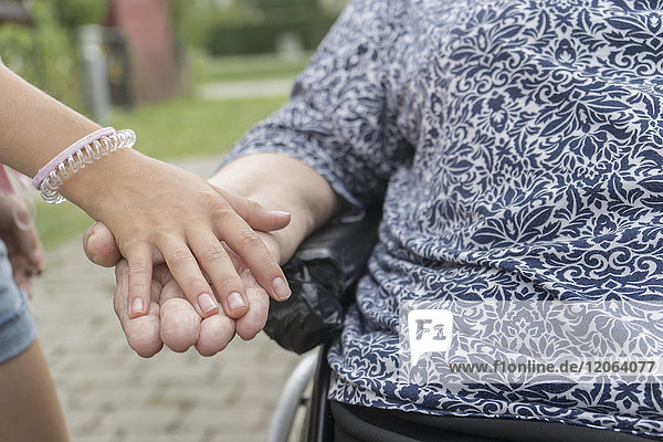 Enkelin hält die Hand der Großmutter im Rollstuhl im Altenheimpark