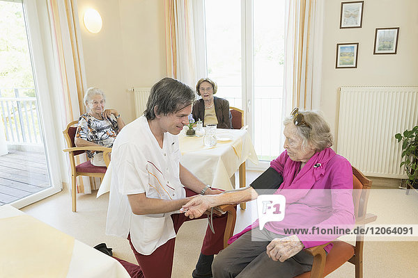 Pfleger kontrolliert Blutdruck einer älteren Frau im Altersheim