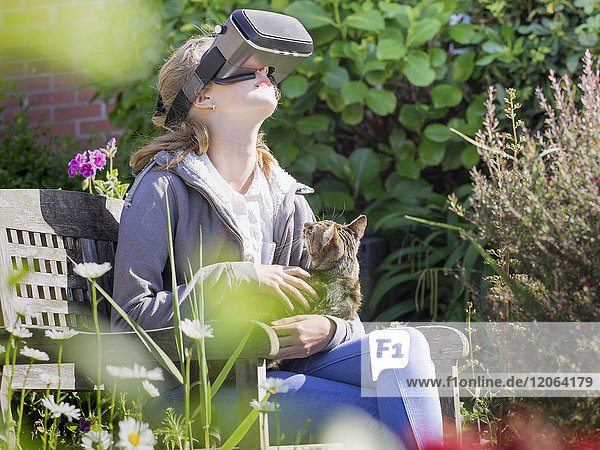 Mädchen mit Virtual-Reality-Headset  während sie mit ihrer Katze auf einer Parkbank sitzt