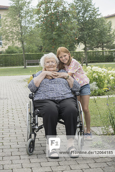 Ältere Frau im Rollstuhl mit Enkelin im Altenheimpark