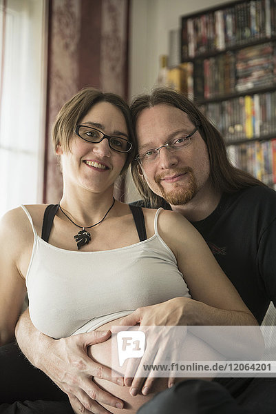 Porträt eines schwangeren Paares mit Händen in Herzform auf dem Bauch
