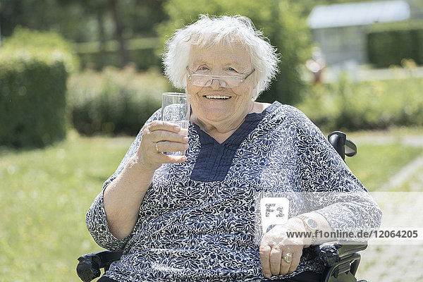 Ältere Frau im Rollstuhl trinkt ein Glas Wasser