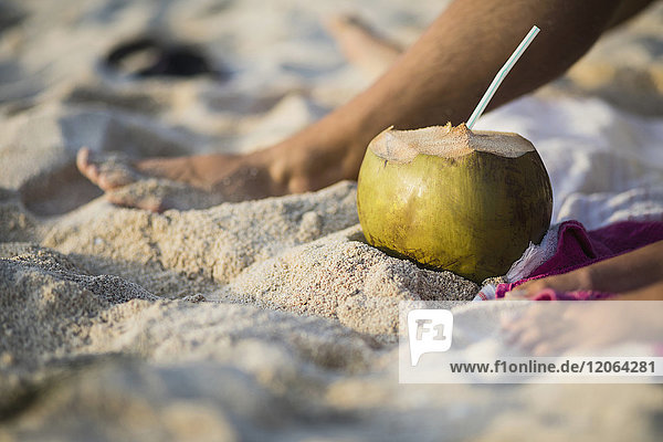 Kokosnuss zwischen den Beinen auf Sand