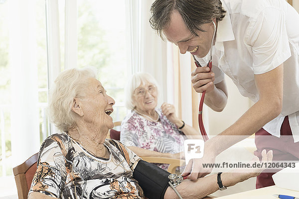 Pflegerin prüft Blutdruck einer älteren Frau im Altersheim
