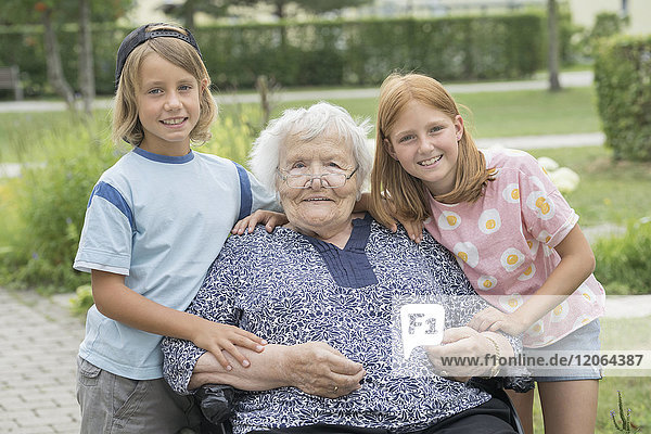 Ältere Frau im Rollstuhl mit Enkelkindern im Altenheimpark