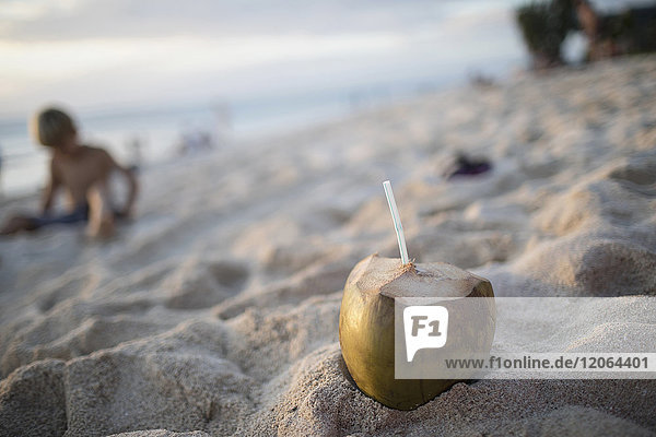 Frische Kokosnuss im Sand mit Trinkhalm