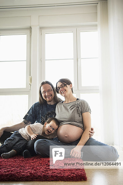 Porträt der Eltern  die auf einem Teppich sitzen  während der Sohn dem Bauch der Mutter zuhört