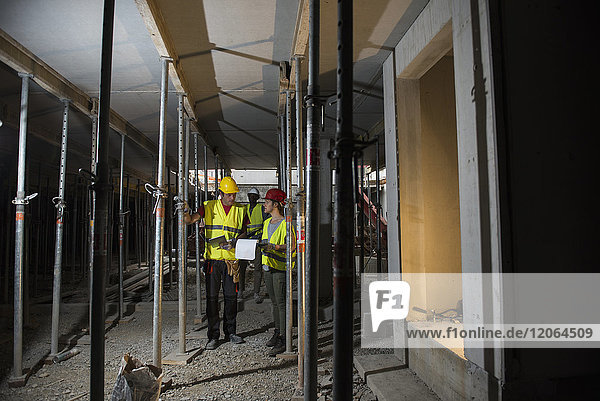 Bauarbeiter mit Architekturplan und digitalem Tablet im Keller einer Baustelle