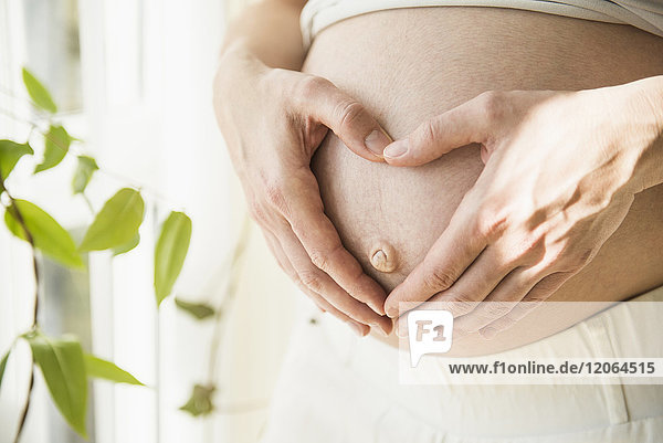 Schwangere Frau mit Händen auf dem Bauch in Herzform