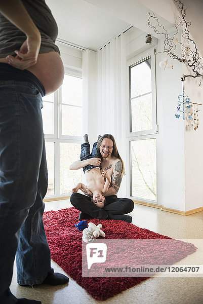 Pregnant mother looking at father and son playing on carpet