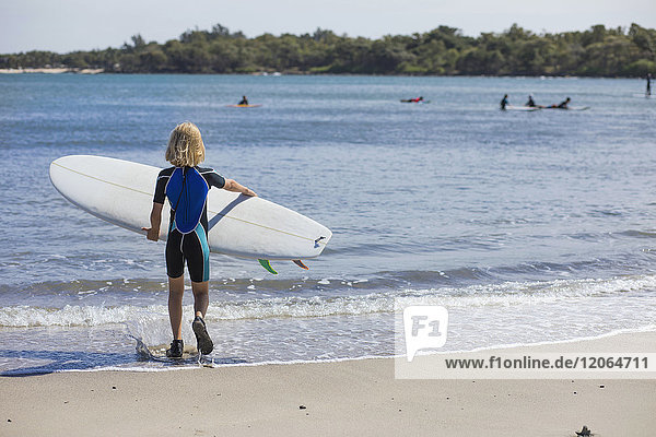 Rückansicht eines Mädchens mit Surfbrett am Strand