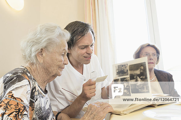 Hausmeisterin betrachtet Fotos mit älteren Frauen im Altersheim