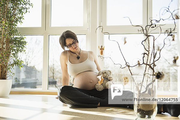 Schwangere Frau mit Teddybär auf dem Boden sitzend