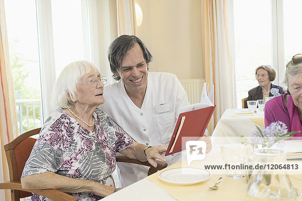 Caretaker reading a book with senior woman at rest home