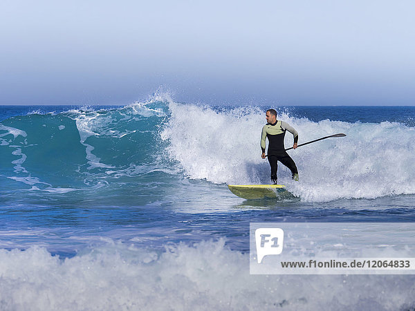 Mann surft mit einem Stand Up Paddling Board am Sopelana Strand