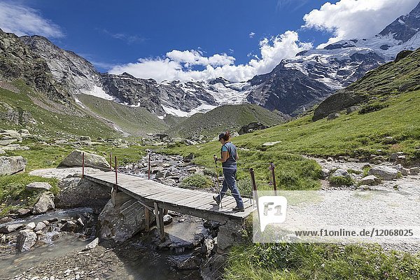A trekker crosses a small wooden bridge near the Zamboni Zappa refuge at the foot of the East face of Monte Rosa Massif (Macugnaga Anzasca Valley Verbano Cusio Ossola province Piedmont Italy Europe).