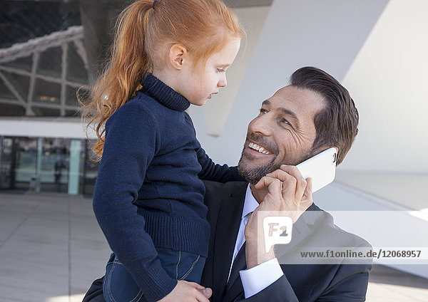 Mann telefoniert  mit Kind auf dem Arm